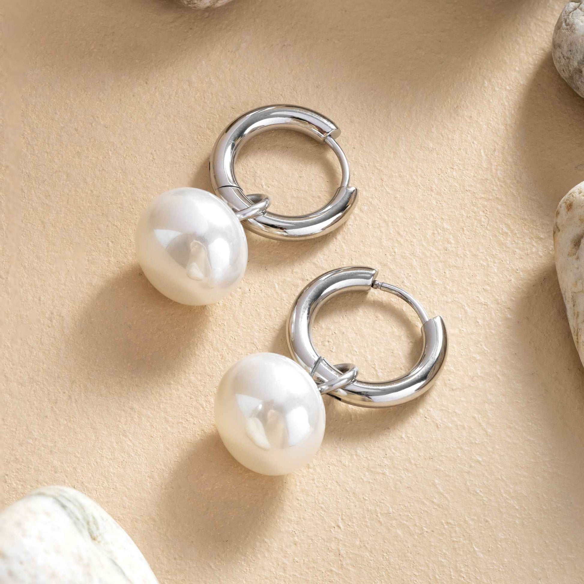 Silver hoop earrings with pearls on a beige surface