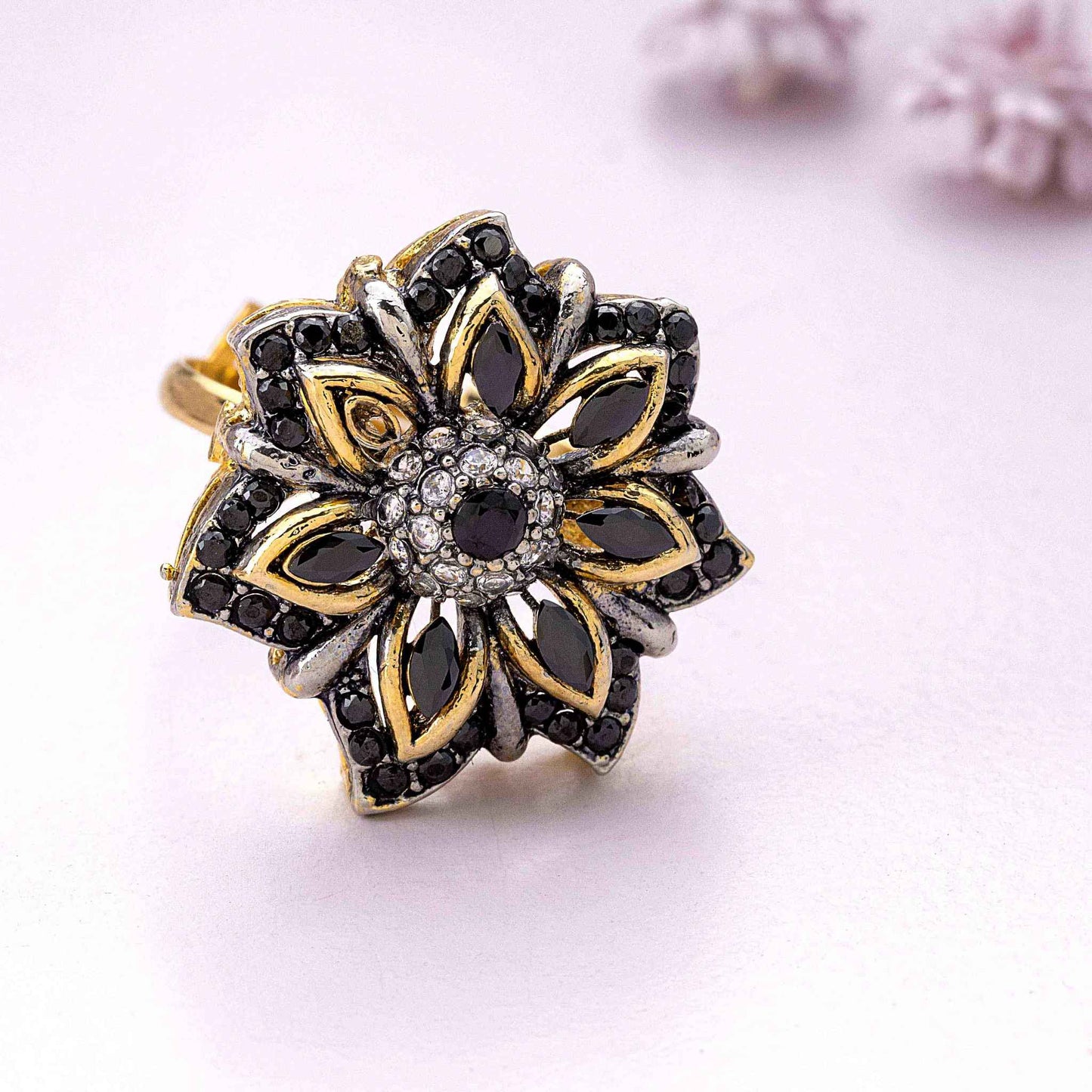 Gold and silver floral ring with black gemstones on a light pink background