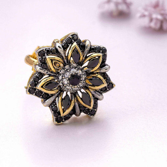 Gold and silver floral ring with black gemstones on a light pink background