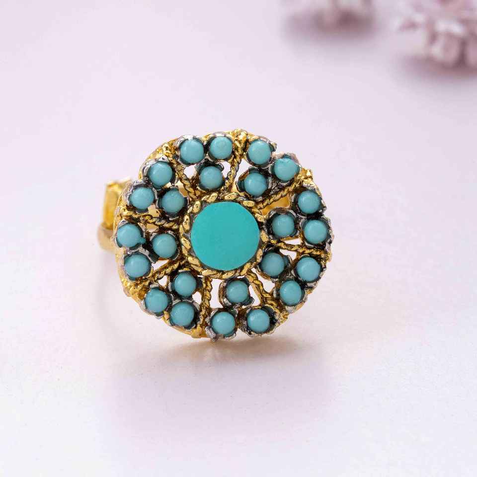 Turquoise ring with gold accents on a light pink background