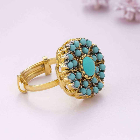 Turquoise ring with gold accents on a light pink background